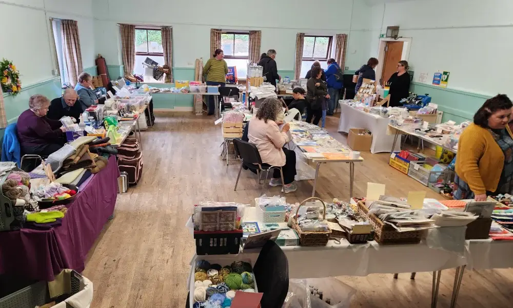 Community hall with tables displaying crafts and supplies, people seated and browsing.